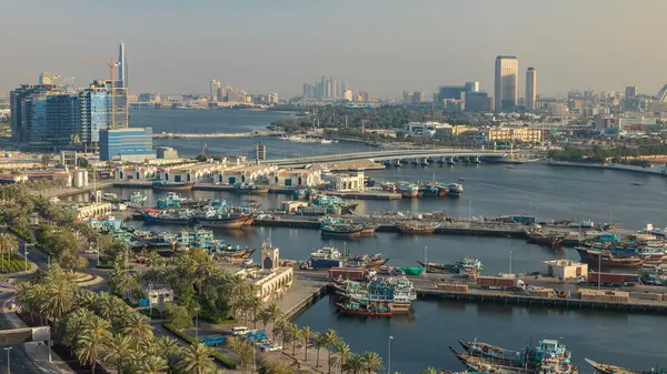 Dubai deresi zaman çizelgesi, limanda tekne ve gemi, sakin su ve günbatımında modern binalar. Yukarıdan yol boyunca trafik ve ağaçlarla hava manzarası