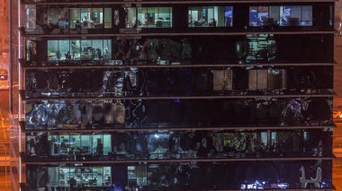 Ofis gökdeleni gece geç saatlerde iç ışıklar açıkken ve insanlar gece vardiyasında çalışırken. Yukarıdan birçok pencereye sahip havadan yakın görüntü
