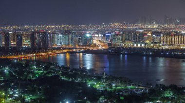 Dubai Creek, Deira 'da, Dubai, Birleşik Arap Emirlikleri' nin arka planında, yeşil ışıklı park ve yolun yanındaki gece şehri.