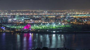 Aydınlatılmış modern şehrin ışıklarının olduğu golf sahası Dubai Deresi 'ndeki suya yansıyan yansıma gece zaman ayarlı havaalanı arka planda Birleşik Arap Emirlikleri.