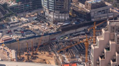 Dubai zaman diliminde sarı vinci olan yüksek binalar inşa ediliyor. Şehir merkezinde sabah hava görüntüsü. Traktörler ve buldozerlerle bodrumda.