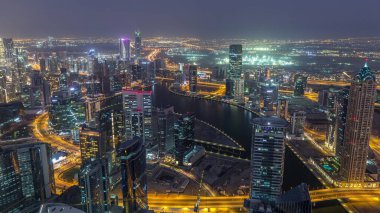 Dubai'deki iş bölümü kulelerinin panoramik havadan görünümü gece geçiş saati. Gün batımından sonra yapım aşamasında olan bazı gökdelenler, kanal ve yeni kulelerin çatı görünümü.