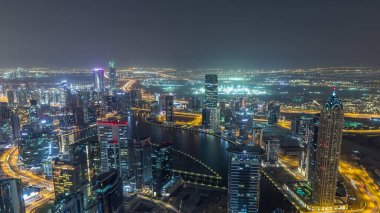 Dubai gece zaman atlamalı iş bölümü kuleleri panoramik havadan görünümü. Yapım aşamasındaki bazı ışıklı gökdelenlerin, kanalın ve yeni kulelerin çatı görünümü.