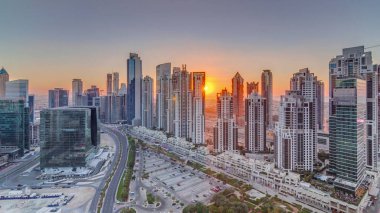 Günbatımında Business Bay, Dubai, Uae 'de bulunan birçok gökdelenle modern yerleşim ve ofis kompleksi. Körfez Bulvarı Parkı 'nın yanındaki büyük otoparkta arabalar ve trafik vardı.
