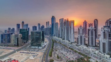Günbatımında Business Bay, Dubai, Uae 'de bulunan birçok gökdelenle modern yerleşim ve ofis kompleksi. Körfez Bulvarı Parkı 'nın yanındaki büyük otoparkta arabalar ve trafik vardı.