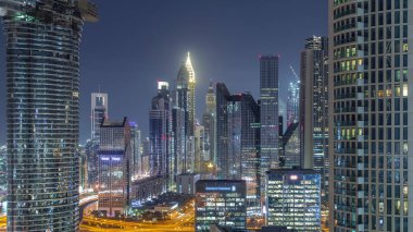 Dubai Finansal Merkezi semti, aydınlatmalı modern gökdelenler, gece zaman çizelgesi. Şehir merkezinden hava görüntüsü caddelerde ve kavşakta trafik var