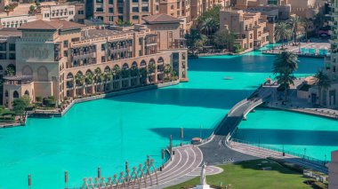 İnsan yapımı göl üzerindeki köprünün havadan yakından görünümü ve Dubai şehir merkezinde el anıtı sabah timelapse ile parkta yürüyen bazı insanlar, Birleşik Arap Emirlikleri.