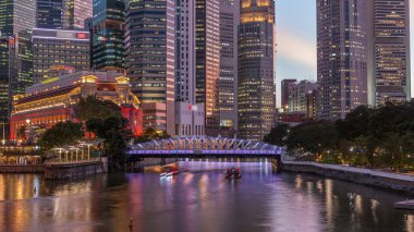 Singapur gökdelenleri beyaz Anderson Köprüsü ve Escplanade Park yakınlarındaki birkaç finans bölgesi kulesi ile gökdelenden geceye geçiş zamanı. Her iki tarafta da yeşil yapraklar var..