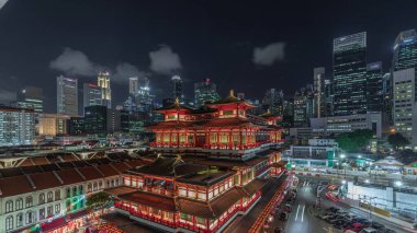 Arka planda şehrin ufuk çizgisi olan Singapur Çin Mahallesi 'nde gece vakti Buda Dişi Kalıntısı Tapınağı canlanır. Tapınak gökdelenler ve kulelerle aydınlık