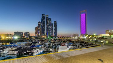 Al Bateen marinası Abu Dabi. Gün batımından sonra tekneler ve arka planda aydınlatmalı modern gökdelenler.