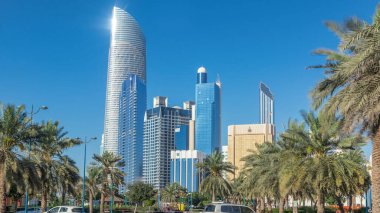 Abu Dabi 'deki sahil şeridi boyunca uzanan Corniche Bulvarı plajı parkında arka planda gökdelenler var. Aile parkından görüntü. Avuçlar yana. Güneşli bir günde mavi gökyüzü