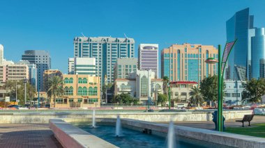 Abu Dabi 'deki sahil şeridi boyunca uzanan Corniche Bulvarı plajı parkında arka planda gökdelenler var. Aile parkından görüntü. Çeşme yan tarafta. Güneşli bir günde mavi gökyüzü