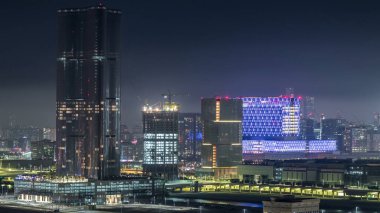 Abu Dabi 'deki Al Reem ve Al Maryah Adası' ndaki gökdelenler. Al Reem Adası 'ndan ışıklandırılmış binaları olan havadan şehir manzarası. Hastane yakınındaki yolda trafik vardı.