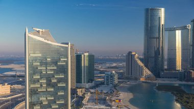 Abu Dabi 'deki Al Reem Adası' ndaki modern binalar yukarıdan zaman dilimi. Akşamları Al Reem Adası 'nın havadan görünüşü sudaki ve uzun gölgelerdeki binaların yansımasını gösteriyor..