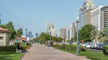 Abu Dabi 'deki sahil şeridi boyunca uzanan Corniche Bulvarı plajı parkında arka planda gökdelenler var. Lake Park 'ın manzarası. Avuçlar yana. Güneşli bir günde mavi gökyüzü