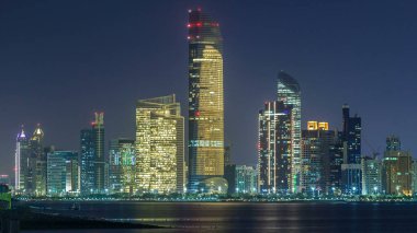 Abu Dabi Skyline 'ın panoramik görüntüsü ve gece vakti deniz manzarası, Birleşik Arap Emirlikleri. Aydınlatılmış gökdelenli Corniche manzarası