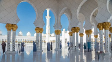 Birleşik Arap Emirlikleri 'nin başkenti Abu Dabi' deki Şeyh Zayed Büyük Camii zaman çizelgesi. Sütunlar arasında yürüyen insanlar. Güneşli bir günde mavi gökyüzü