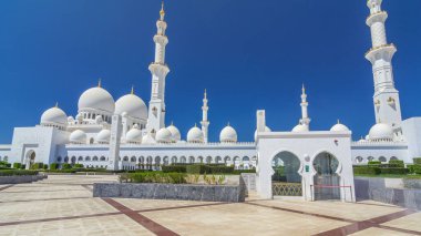 Birleşik Arap Emirlikleri 'nin başkenti Abu Dabi' deki Şeyh Zayed Büyük Camii zaman atlaması. Kubbeler ve minarelerle yan manzara. Ön planda çalılıklar. Güneşli bir günde mavi gökyüzü