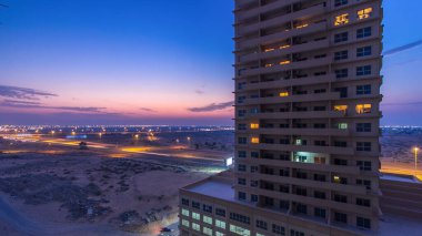Ajman 'da çatıdan gece kuleye kule ve kavşakta trafik olan şehir manzarası. Birleşik Arap Emirlikleri 'nde gün batımından sonra aydınlanan binaların hava manzarası.