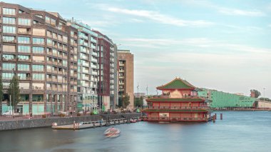 Sudaki pagoda şeklinde bir Çin restoranının hipervanesi, tarihi şehir merkezi binalarının ve günbatımında modern mimarinin arka planına karşı kurulur. Amsterdam, Hollanda