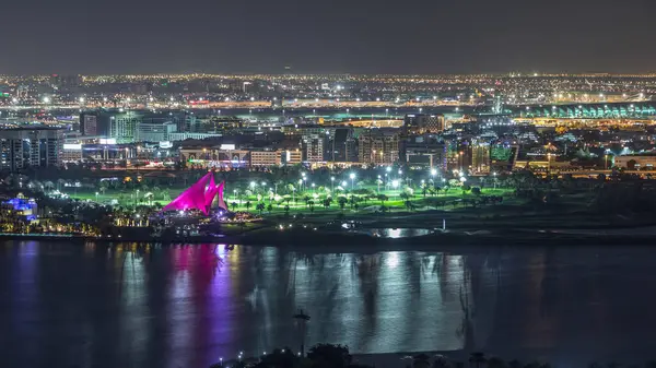 Aydınlatılmış modern şehrin ışıklarının olduğu golf sahası Dubai Deresi 'ndeki suya yansıyan yansıma gece zaman ayarlı havaalanı arka planda Birleşik Arap Emirlikleri.