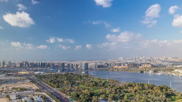Güneşli bir günde Deira ve Dubai derelerindeki binaların hava panoramik görüntüsü mavi gökyüzünde bulutlar Timelapse ve Dubai şehrinin arka planında gökdelenler, Birleşik Arap Emirlikleri