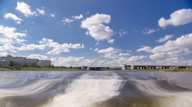 Astana, Kazakistan. Keyif teknesinden Astana 'da Ishim nehrinde hareketli bir seyahat görüntüsü. Mavi gökyüzü ve bulutlarla dolu bir yaz gününde. Bulanık hareket