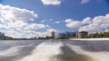Astana, Kazakistan. Keyif teknesinden Astana 'da Ishim nehrinde hareketli bir seyahat görüntüsü. Mavi gökyüzü ve bulutlarla dolu bir yaz gününde. Bulanık hareket