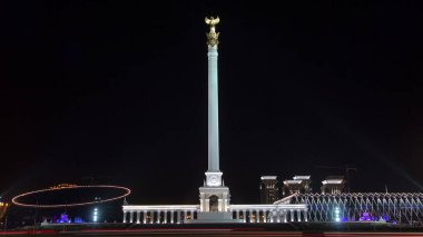 Stele anıtı Kazak Eli ve kuş Samruk geceleri ve Bağımsızlık Sarayı hiperhız ve trafik ön planda. Nur-Sultan şehri, Kazakistan