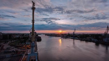 Shipyard with historical cranes in the industrial part on a riverside during sunrise aerial timelapse. Plants and factories around. Colorful sky at the morning