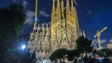Sagrada Familia: İspanya 'nın Barcelona kentindeki Iconic Roma Katolik Kilisesi' nin Gündüzden Geceye Geçiş Süreci. Kuleler ve Turnalar Yakınlardaki Gölün Huzurlu Sularında Yansımaya Karşı Duruyor