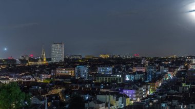 Brüksel üzerinde, Schaerbeek 'teki tren istasyonuna yakın gökdelende hava gecesi panoraması. Yerleşim yerleri, aydınlatılmış Saint-Servais Kilisesi Belçika 'nın başkentindeki kırmızı çatılarla çevrili.