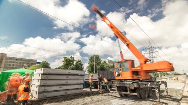 Yol inşaatı zamanında vinçten vince beton plakaları boşaltıyordum. Kask ve turuncu üniformalı endüstriyel işçiler.