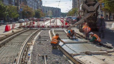 Beton döşeme ve karayolu inşaatı. Turuncu üniformalı birçok işçi ve şehir trafiği. Tramvay raylarının yeniden inşası