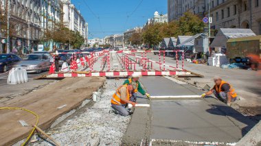 Beton, turuncu üniformalı ve mikser makineli işçilerle bir şehir merkezinde yol inşaatında çalışıyor. Tramvay raylarının yeniden inşası