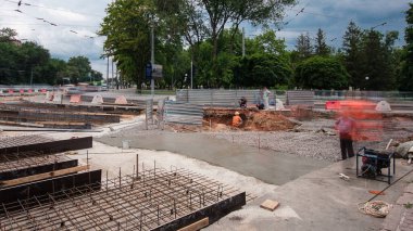 Tramvay rayları onarımı ve bakım zamanı olan bir yol inşaatı. Kavşağın ortasında beton işi ve mikser var. Demiryolu raylarının birçok işçiyle değiştirilmesi