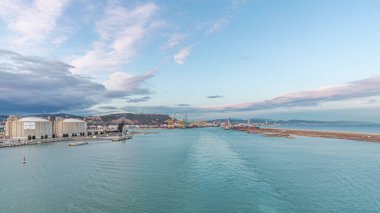 Gün batımında açık denizde yelken açan gemiden dalgalı ve limanlı deniz manzarası. Barselona kıyısı, İspanya