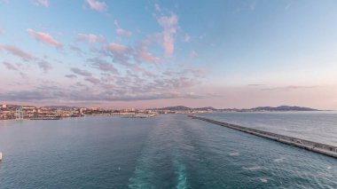 Gün batımında açık denizde yelken açan gemiden dalgalı ve limanlı deniz manzarası. Marsilya kıyısı, Fransa