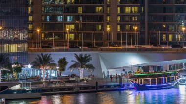 Yat ve tekne shoping mall kalıyor ve Dubai Marina bölge gece timelapse bir köprü altında geçen turist. Işıklı bina ve sahil ile hava üstten görünüm