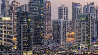 Lüks Dubai Marina Kanalı 'ndan geçen tekneler ve gece gündüz restoranlarla gezinti günbatımından sonra aydınlık gökdelenlerle yukarıdan manzaralı. Dubai, Birleşik Arap Emirlikleri