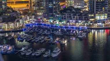 Lüks Dubai Marina Kanalı 'ndan geçen tekneler, yatlar ve restoranlarla dolu bir gezinti yeri gece zaman çizelgesi, yukarıdan aydınlık gökdelenleri olan bir manzara. Dubai, Birleşik Arap Emirlikleri