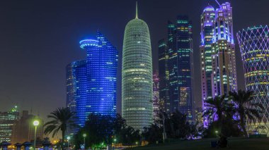 Doha 'nın yüksek katlı bölgesinde gece vardiyası, parktan görülmüş. Batı körfezinde aydınlatılmış gökdelenler ve palmiyeler