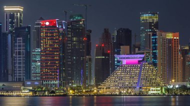 Doha şehir merkezi ufuk çizgisi günden geceye geçiş zamanı, Katar, Orta Doğu. Batı Körfezi 'ndeki aydınlık gökdelenler Körfez suyuna yansıyor. MIA parkından görüntü