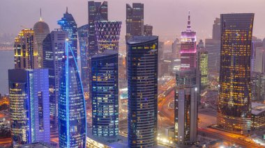 Batı Körfezi bölgesinin ufuk çizgisi Doha 'da günden geceye geçiş zamanı, Katar. Günbatımından sonra modern gökdelenlerin çatıdan görünüşü aydınlandı. Yolda trafik vardı.