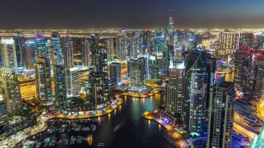 Dubai Marina 'da yatlar ve gece gündüz hava geçiş panoramik zaman dilimi. Mavi gökyüzü ile açık bir akşamda parlak ışıklar ve en yüksek gökdelenler. Gün batımından sonra yukarıdan görünüm