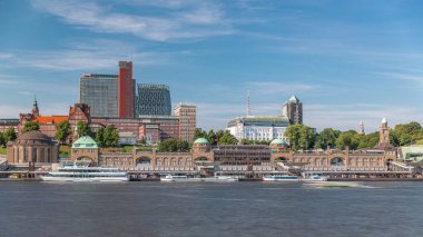 Almanya 'nın Hamburg kentinde feribotlarla St. Pauli İskelesi' nin (Landungsbrucken) Skyline zaman çizelgesi. İkonik saat kulesi, yat limanına yanaşan gemiler ve bulutlu mavi gökyüzünün altındaki limanın panoramik manzarası.