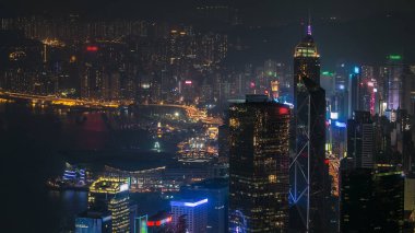 Geceleri Hong Kong şehrinin gökyüzü zaman çizelgesi. Victoria Limanı ve ışıklarla aydınlatılan ünlü gökdelenler sergi merkezi ve kuleleri olan dağın tepesinden izleniyor..