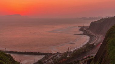 Lima 'nın Miraflores yakınlarındaki Lima' nın Sahil Çizgisi 'nin gün batımı görüntüsü turuncu ışık, Lima, Peru. Trafikli yol ve okyanuslu sahil.