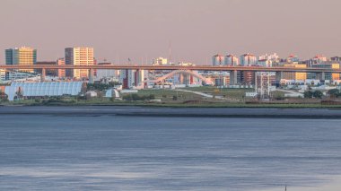 Lizbon 'daki Park Tejo ve River Timelapse' ın arka planında Milletler Bölgesi Modern Mimari Parkı var. Percurso Ribeirinho de Loures 'ten Vasco da Gama Köprüsü
