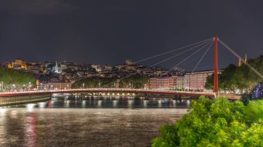 Saone Nehri üzerindeki kırmızı asma köprü ile Lyon 'un şehir manzarasının gece zaman çizelgesi, gece boyunca aydınlatılmış deniz kenarı suya yansıdı. Fransa